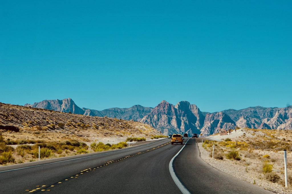 Open road with cars and scenic mountain backdrop under clear blue sky in desert landscape