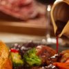 Traditional Sunday roast with Yorkshire pudding and gravy being poured, served with vegetables and potatoes