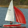 Red and white sailboat gliding on a lake with lush green trees in the background on a clear day
