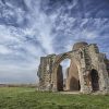 Ancient stone ruins under a blue sky in a grassy field, showcasing historical architecture in the UK landscape