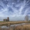 Ancient English ruin by marshland under dramatic cloudy sky in countryside landscape