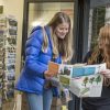 Two women in a visitor centre reading a brochure, surrounded by postcards and nature art