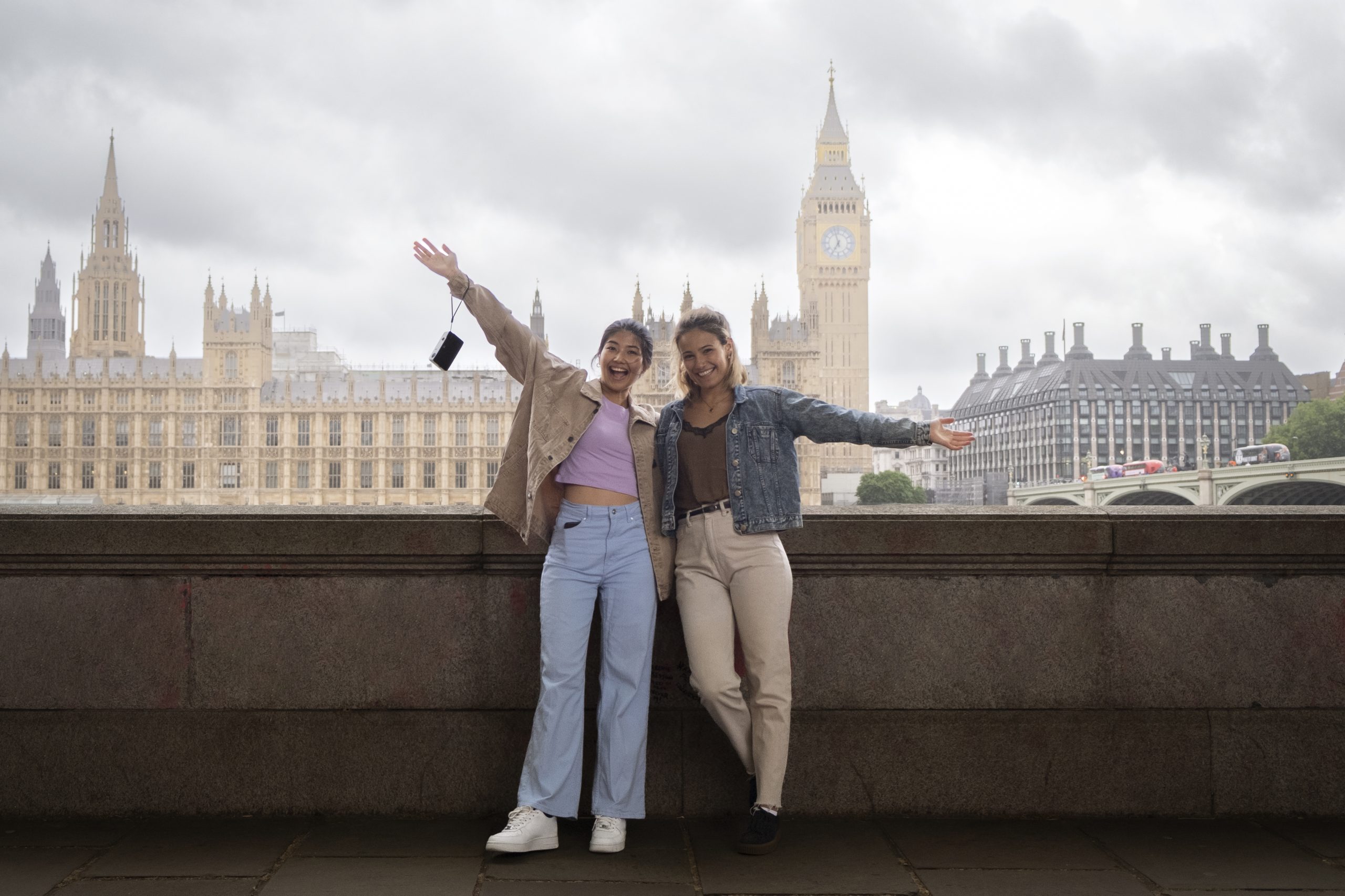Two smiling women posing with arms outstretched in front of Big Ben and the Houses of Parliament in London, capturing a joyful moment