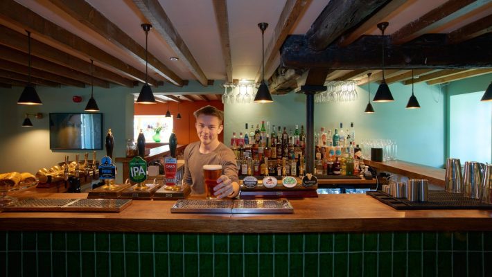Bartender serving pint in cosy UK pub with wooden beams and well-stocked bar