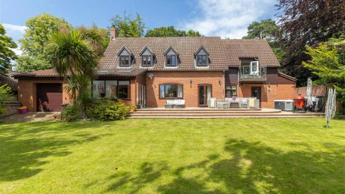 Spacious brick house with large garden and patio furniture under a clear sky in a suburban area of the UK