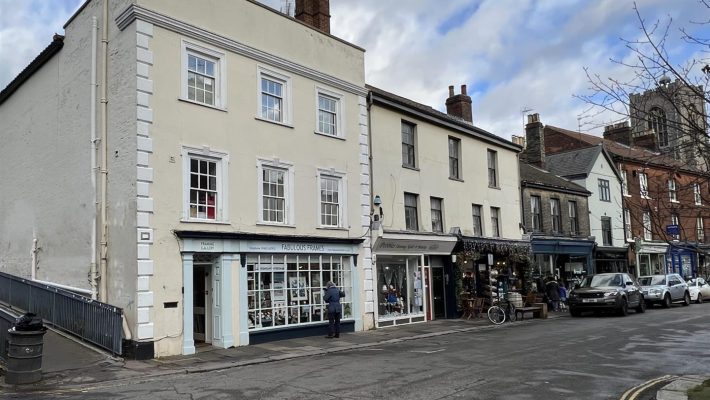 Charming UK high street with historic buildings, shops, and a parked car on a cloudy day