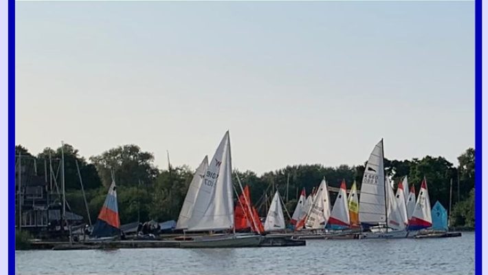 Sailboats anchored on a tranquil lake with a backdrop of lush greenery and a clear sky