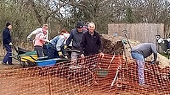 Group of volunteers working on a community garden project with wheelbarrows and tools in an outdoor setting