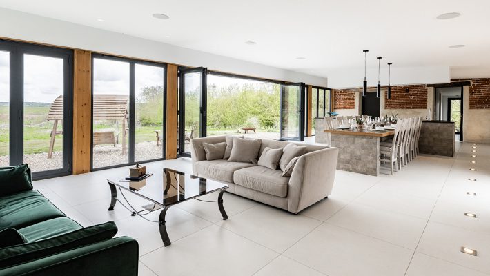 Modern open-plan living room with large windows, elegant sofas, and a stylish kitchen overlooking a scenic landscape