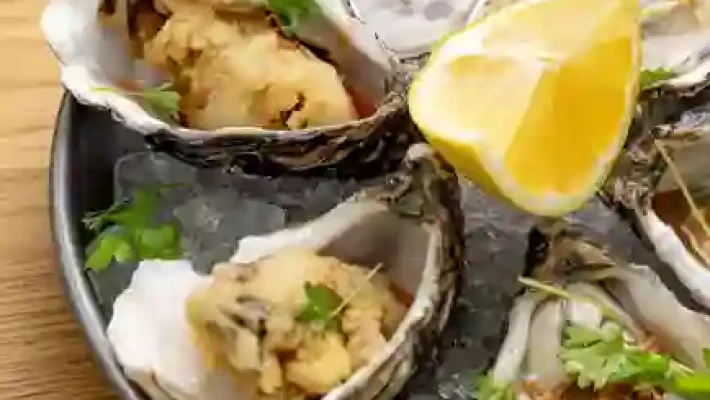 Fresh oysters on ice with lemon wedge, garnished with herbs, served on a plate for a seafood delicacy presentation