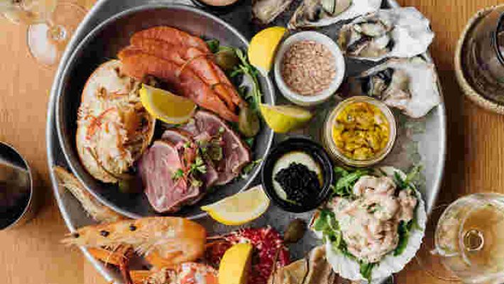 Platter of fresh seafood with prawns, oysters, crab, lemon wedges, and sauces on a round dish atop a wooden table