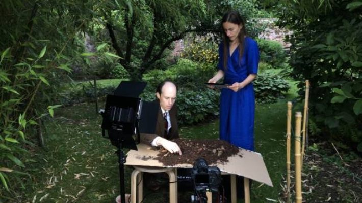 Man and woman conducting soil experiment in a garden setting with camera equipment nearby
