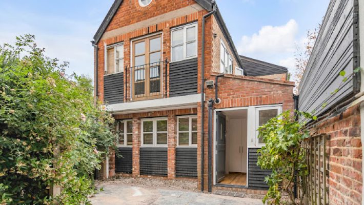 Charming two-storey brick house with lush garden in the UK, featuring large windows and a welcoming entrance path