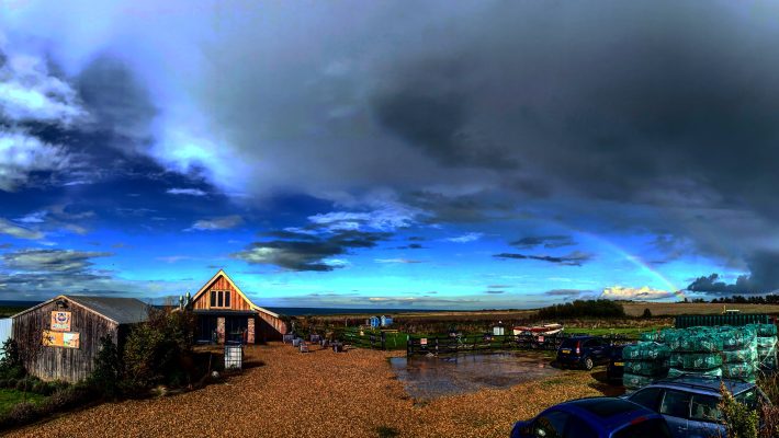 Rural landscape with rustic buildings, vibrant sky, and distant rainbow in the English countryside