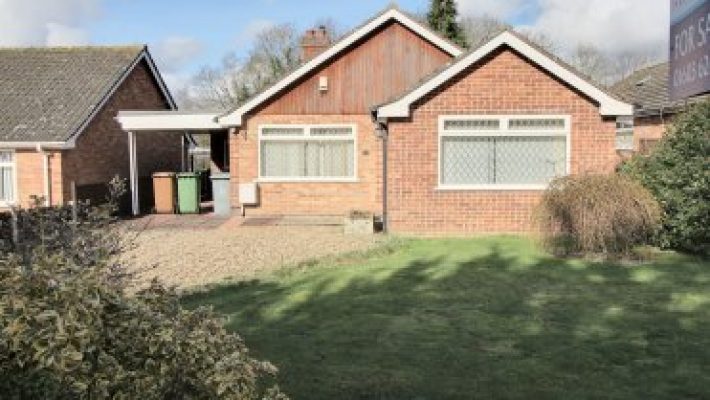 Single-storey red brick house with a well-maintained front garden, under clear blue skies in a suburban setting