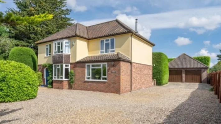 Spacious two-storey house with a gravel driveway, lush greenery and detached garage in a suburban setting