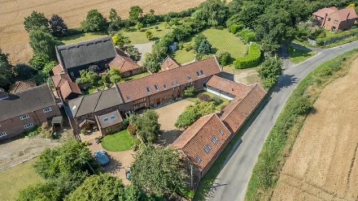 Aerial view of quaint countryside village with red-roofed buildings, lush greenery, and winding road in rural England