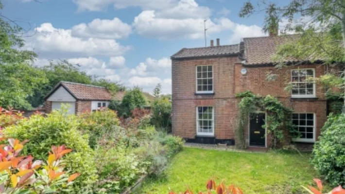 Charming British countryside cottage with lush garden and brick exterior under a blue sky with fluffy clouds
