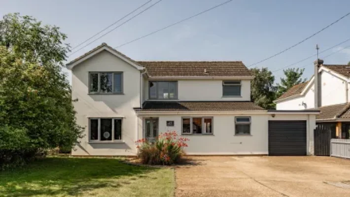 Two-storey suburban house with white facade, pitched roof, garage, and front garden on a sunny day in the UK