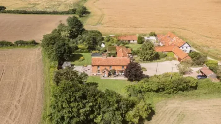 Aerial view of a rural English farmhouse with red roofs surrounded by lush fields and greenery