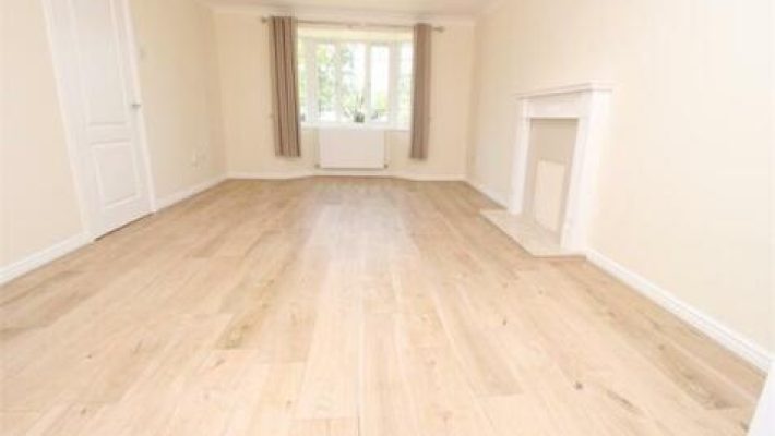 Spacious empty living room with wooden flooring, neutral walls, large window and fireplace in a modern home
