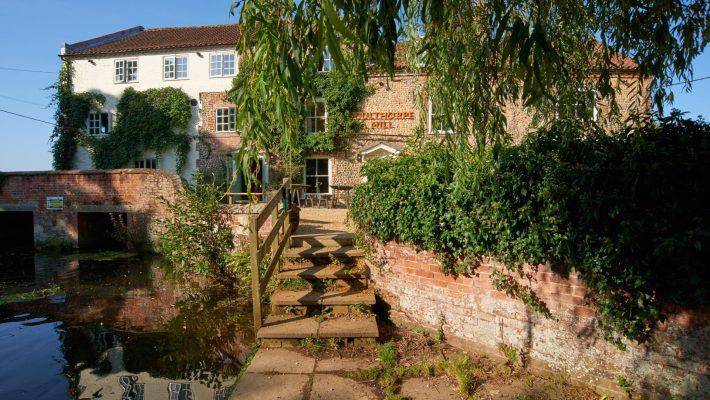 Charming historic mill surrounded by lush greenery and a tranquil waterway in the English countryside