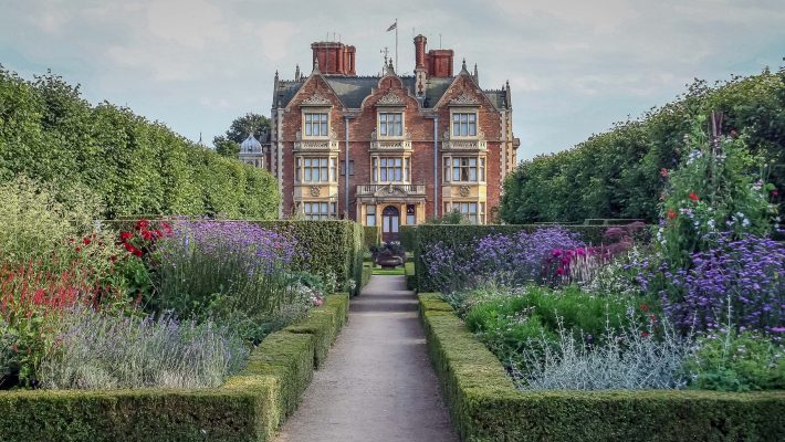 Elegant Victorian mansion with lush gardens and hedges under a cloudy sky in the UK countryside