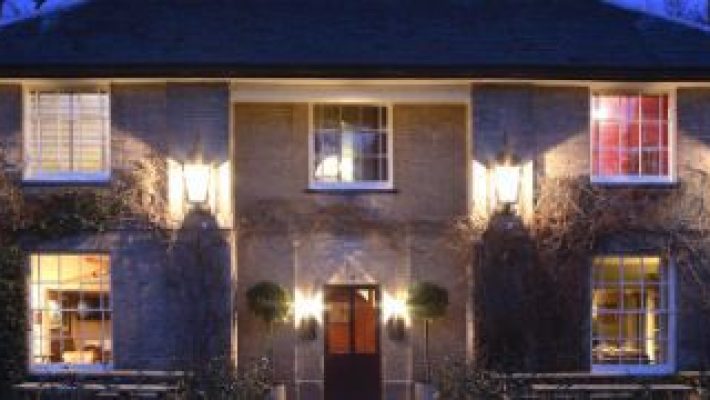 Historic English inn lit up at night, showcasing warm lighting and classic architecture, surrounded by benches and greenery