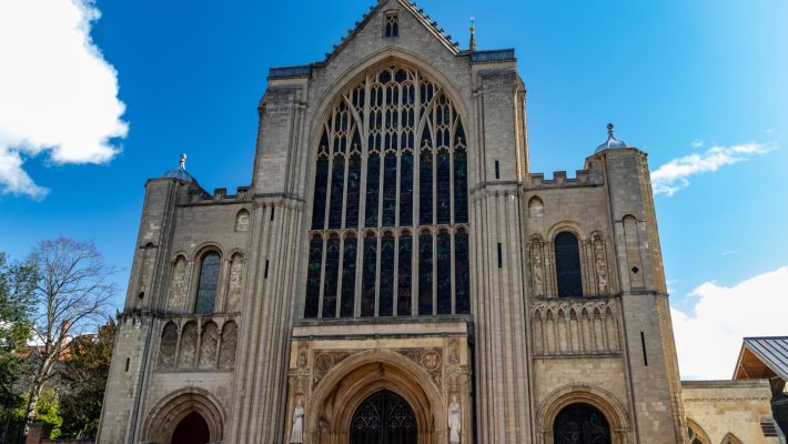 Front view of a historic cathedral with ornate windows and stone carvings under a clear blue sky in the UK