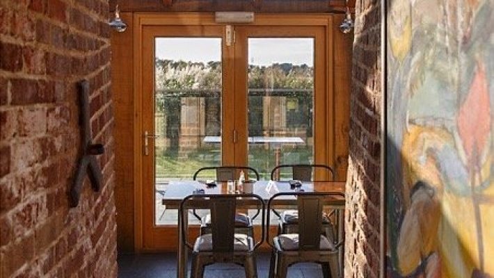 Dining area with metal chairs and wooden doors in a brick-walled space, natural light streaming in from outside