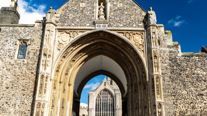 Historic cathedral entrance under a blue sky with intricate stonework and statues in a traditional UK setting