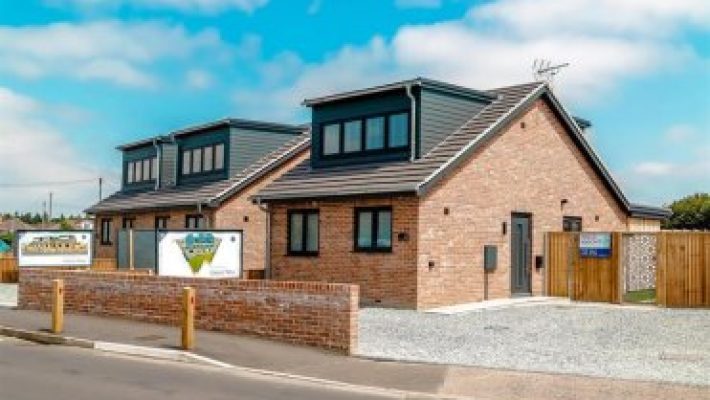 Modern brick homes with slate roofs and driveways in a residential neighbourhood under a clear blue sky