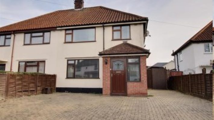 Front view of a semi-detached house with driveway, red brick detail, and brown roof in a residential UK neighbourhood