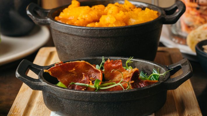 Rustic cast iron dishes with crispy bacon and mashed potatoes served on a wooden board in a cosy dining setting