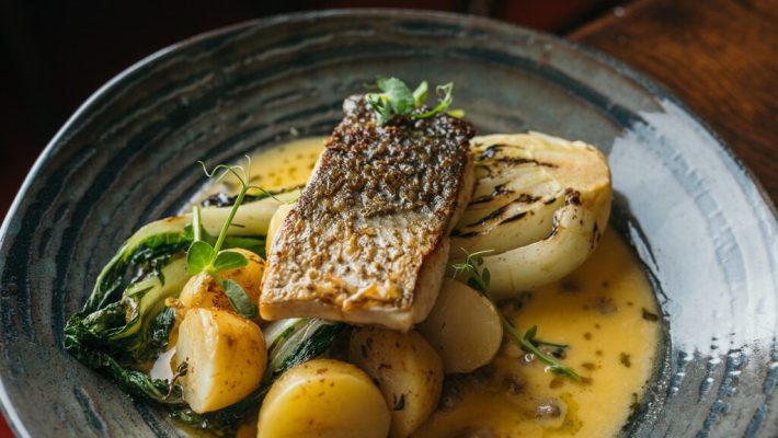 Grilled fish fillet with roasted potatoes, pak choi, and a rich sauce served in a stylish grey dish