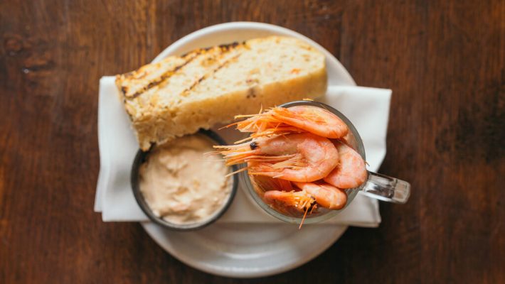 Prawns in a glass with cocktail sauce and garlic bread on a wooden table, top view dining experience