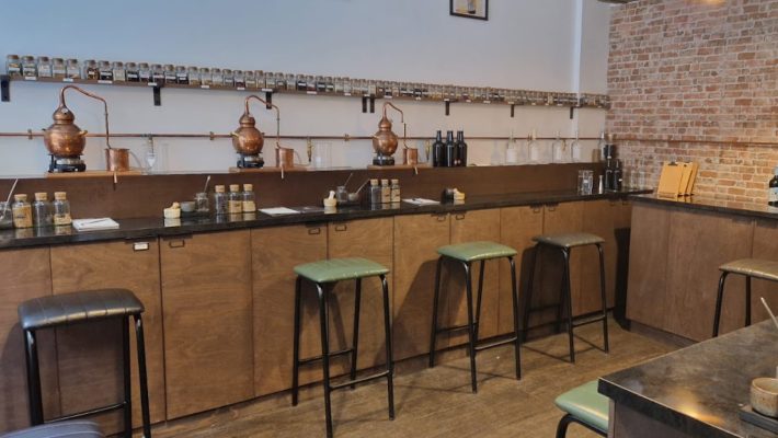 Modern distillery interior with copper stills, glass jars and wooden cabinetry, accented by industrial bar stools