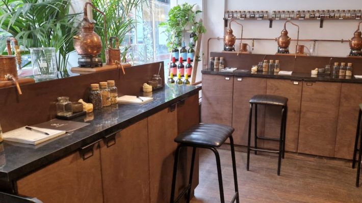 Distillery workshop with copper stills, botanical jars and stools, set in a cosy room with plants and natural light