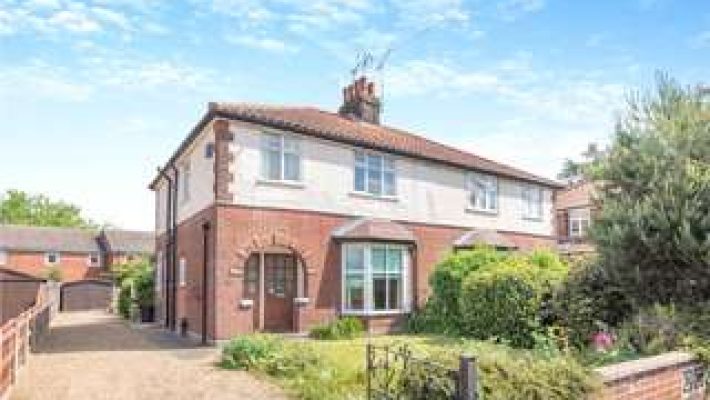 Semi-detached brick house with arched windows and front garden on a sunny day in a residential area