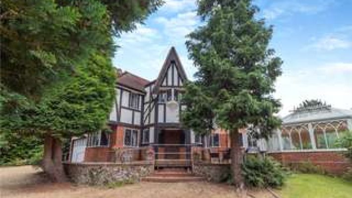 Tudor-style country house surrounded by trees and a garden with clear blue sky