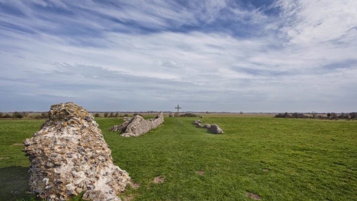 Ancient stone ruins on green countryside landscape under a cloudy blue sky in the UK