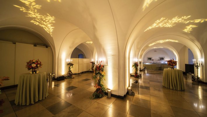 Elegant event venue with arched ceilings, ambient lighting, floral decor, and round tables ready for a special occasion