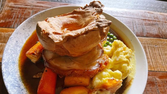 Traditional British roast dinner with Yorkshire pudding, roast beef, potatoes, carrots, peas and gravy on a rustic table