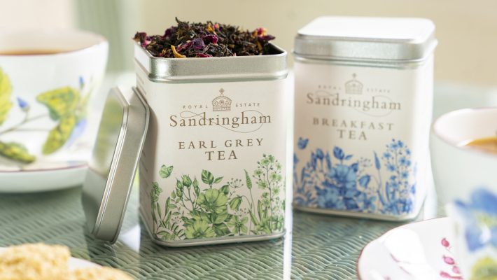 Sandringham Earl Grey and Breakfast Tea tins with floral design on a table with teacups and biscuits