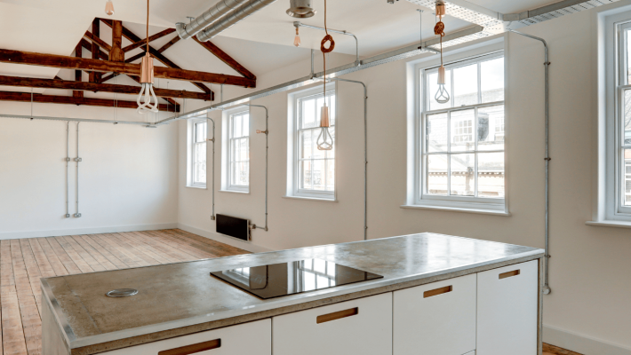 Modern kitchen with exposed beams and ample natural light from large windows in an industrial-style loft conversion
