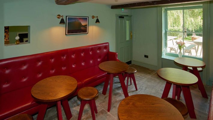 Cosy café interior with red bench seating, round wooden tables, and green walls in a bright room overlooking a garden