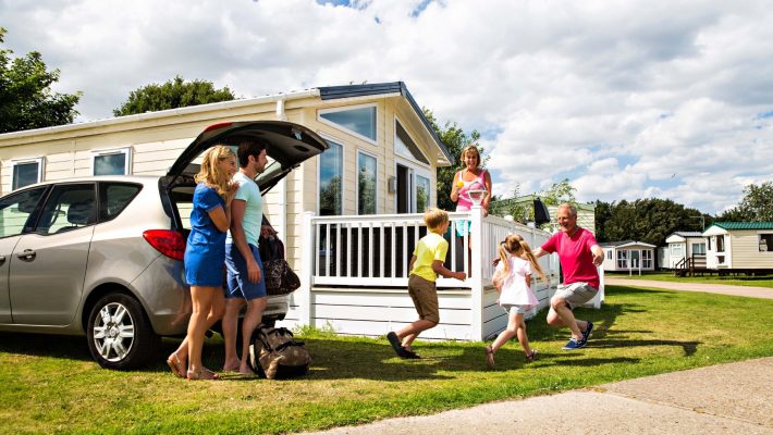 Family enjoying a holiday at a caravan park in summer, unloading car near accommodation under a blue cloudy sky
