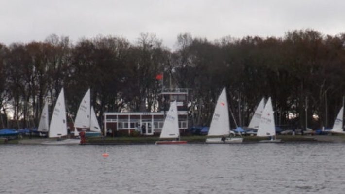 Sailing boats docked by a tree-lined shore on a cloudy day at a scenic lake in the UK
