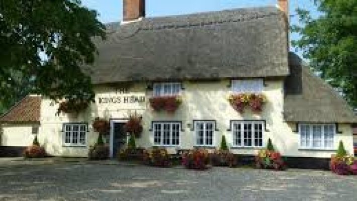 Charming English countryside pub with thatched roof surrounded by colourful flowers and lush greenery