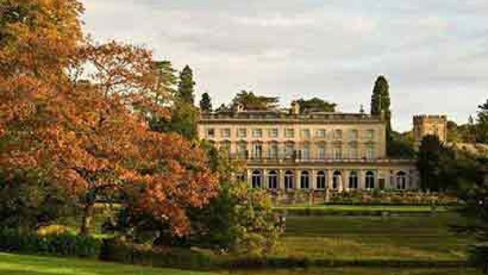 Historic mansion surrounded by lush greenery and autumn trees under a clear sky in the English countryside